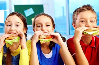 Three children smiling and eating sandwhich