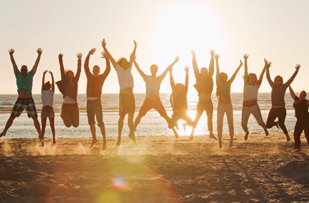 Group of people on a beach jumping up with their hands raised