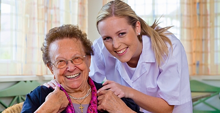 A clincian with her hands on the shoulders of an elderly lady and both smiling