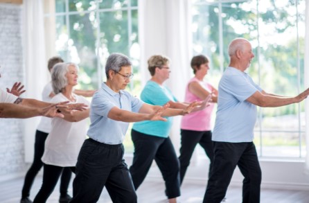 A group of aged men & woman excercising iwth their hands stretched to the front